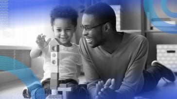 A smiling father and toddler playing with blocks.