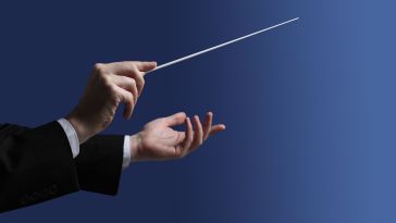 A pair of hands gesture while holding a conductor’s baton.