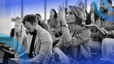 A woman sitting with a group of people is raising her hand to ask a question.