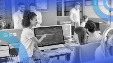 Software developers at an office are gathered around a large computer screen.