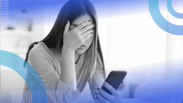 A woman holding a smartphone is covering her eyes and looking frustrated.