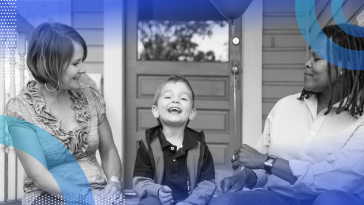 Two moms and their small son sitting on porch steps smiling, while one mom hands the boy a balloon.