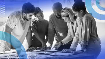 A group of happy and diverse employees are collaborating as they stand at a table.