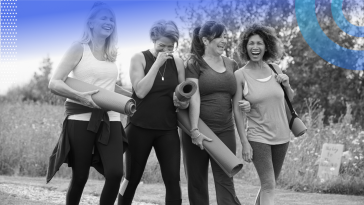 Four women are carrying yoga mats and laughing and talking.