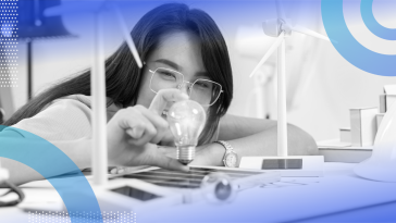 A woman with glasses is holding a light bulb and smiling.