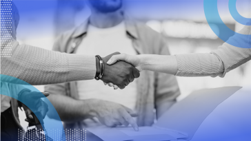 A white and a Black person shake hands over business documents held by a third person