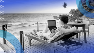 A person is sitting on a lounge chair with a laptop on a patio overlooking an ocean.
