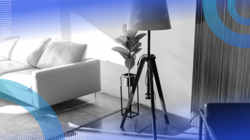 A standing lamp in a living room next to a potteed plant and sofa.