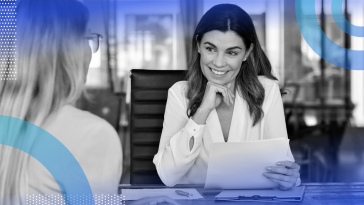 A woman is smiling and looking at a sheet of paper, and another woman sits across from her.