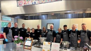 Q2 team members wearing company-branded T-shirts and aprons pose for a group photo at a volunteer event where they provided lunch to those in need.