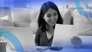 A smiling woman is looking at a paper pay stub.