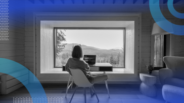 A woman is sitting at a desk that overlooks a calm mountain view.