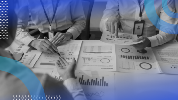 A close-up, neck-down view of three business people poring over graphs and charts at a table.