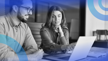 Two coworkers are sitting at a desk and looking at a piece of paper.