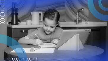 A child sitting at a table doing homework with an iPad propped up in front of her.