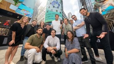 Gynger team members smiling and posing for group photo in front of the Nasdaq stock exchange building display in Times Square in NYC, celebrating their Series A funding round.