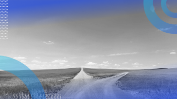 A dirt road the splits into two paths, surrounded by grass on either side with a clear sky above.