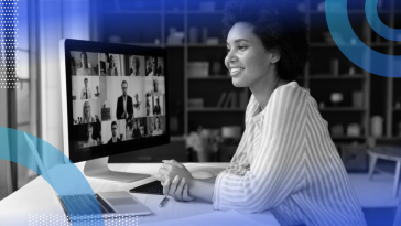 A smiling woman sitting at a desk with a laptop and large computer monitor in front of her.