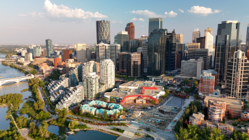 An aerial view of the Calgary skyline on a sunny day, with the Bow River peaking through the left side. 