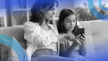 A mother and child sitting on a couch interacting with a smartphone together.