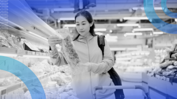 A woman grocery shopping, looking closely at sustainbly packaged vegetables.