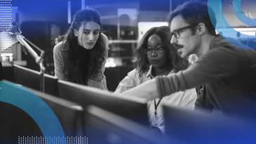 Three software developers collaborating while one points at the desktop screen.