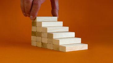 a hand placing a wooden block on top of a stack of wooden blocks