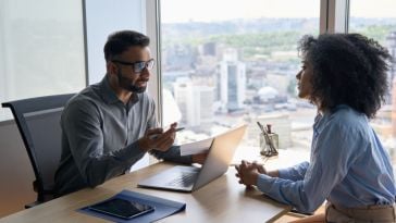 two professionals talking at a desk