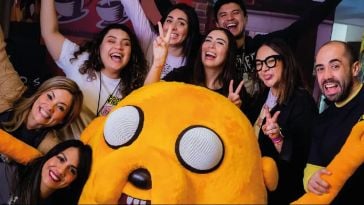 Warner Bros. Discovery team members pose with a large plush character of Jake the Dog from Adventure Time.