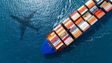 silhouette of a plane flying over a cargo ship