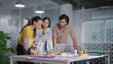 Indian gen z professional business people standing at indoor office use laptop listening project meeting discussion. 