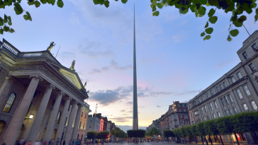 The Dublin Spire monument is visible against an early sunset.