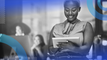 A woman smiling down at her tablet with colleagues in the background behind her.