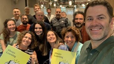 Udemy employees pose for a group selfie holding signs that read “Always Learning.”