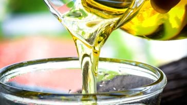 A close up of cooking oil being poured out of a glass pitcher and into another glass dish.