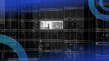 A man talks on his phone in an office building in the lone illuminated window