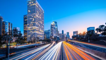 Cars zip down a motorway becoming nothing but streams of light that converge in the center, bordered by high rises.