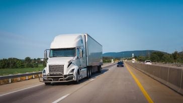 A large white semi-truck drives down a highway.