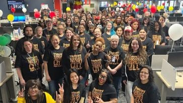 A large group of TrueML employees post in an office wearing matching shirts and surrounded by balloons.