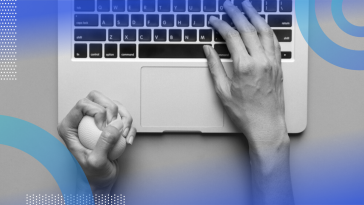 An aerial view of a pair of hands on a laptop keyboard, the right hand typing while the left hand squeezes a stress ball.