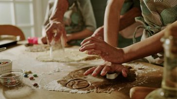 A photo of a family cutting cookie shapes from dough on a floured kitchen table.