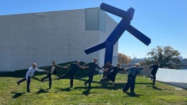 The Nisos executive leadership team stands on the lawn of the Kennedy Center for the Performing Arts in Washington, D.C., in front of “Blue,” a blue geometric modern art statue by Joel Shapiro.  