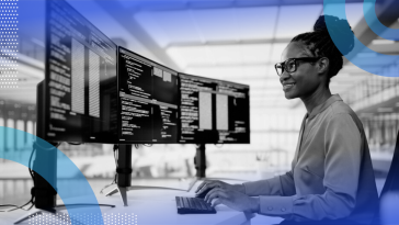 A smiling woman software engineering writing code at her computer with three monitors.