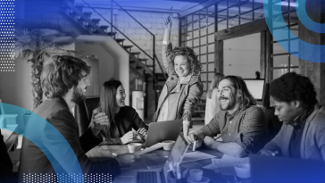 A group of young professionals laughing and exchanging ideas, with the woman in the middle of the group raising her arm triumphantly in the air.