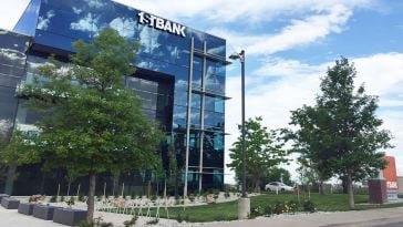 A photo of FirstBank’s corporate office building; its glass exterior reflects the blue sky, clouds and trees. 