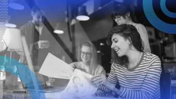 A group of young marketing and PR professionals smiling while looking over paperwork together.