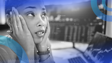 A close-up shot of a stressed tech employee with both hands on either side of her face in front of two monitors with code on them.