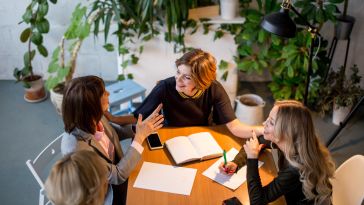 Four team members chat while working on a project together in an office