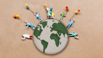 A photo of miniature figures around a cut out of a globe, holding balloons to show the idea of a mission-driven company and connection. 