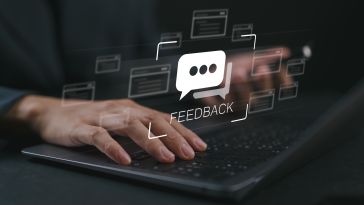 A photo of hands at a laptop with holographic feedback icons over them to show the concept of employee performance reviews. 